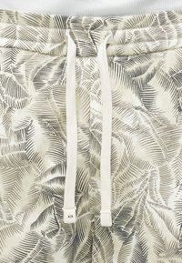 Ελαφρύ, κρεμίζων ύφασμα με λεπτομερή μαύρο σχέδιο φύλλων. Διαθέτει μέση με κορδόνι και μια μικρή ετικέτα λογότυπου.