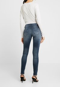 Úzké modré džíny s vybledlým wash, zadními kapsami a vysokým pasem. Nosené s světle šedým topem s dlouhým rukávem a otevřenými podpatky.