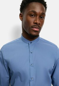 Hellblaues Langarmhemd mit Stehkragen, das eine glatte Textur und Knopfdetails entlang der Vorderseite aufweist.