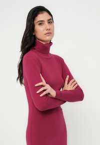 Φόρεμα με εφαρμοστό ζιβάγκο σε βαθύ ματζέντα χρώμα, φτιαγμένο από απαλό πλεκτό ύφασμα. Μακριά μανίκια και μινιμαλιστικός σχεδιασμός με λιτή σιλουέτα.