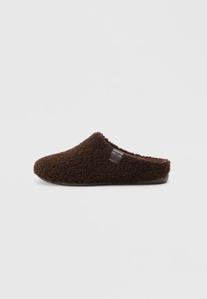 Chausson marron et moelleux à enfiler avec une texture douce, un bout arrondi et une légère arche. Présente un petit logo sur le côté.