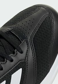 Gros plan sur la pointe d'une basket noire avec tissu en mesh, surcouches en cuir perforé, lacets noirs et semelle intermédiaire blanche.
