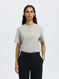 Lichtgrijze T-shirt met korte mouwen en een ronde hals, gecombineerd met zwarte, op maat gemaakte broek. De stof lijkt zacht met een gladde textuur.