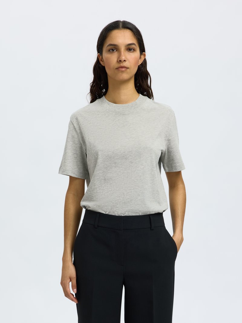 Lichtgrijze T-shirt met korte mouwen en een ronde hals, gecombineerd met zwarte, op maat gemaakte broek. De stof lijkt zacht met een gladde textuur.