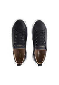 Coppia di sneakers nere in pelle con suole bianche, lacci neri e rivestimento interno beige, viste dall'alto su sfondo bianco.