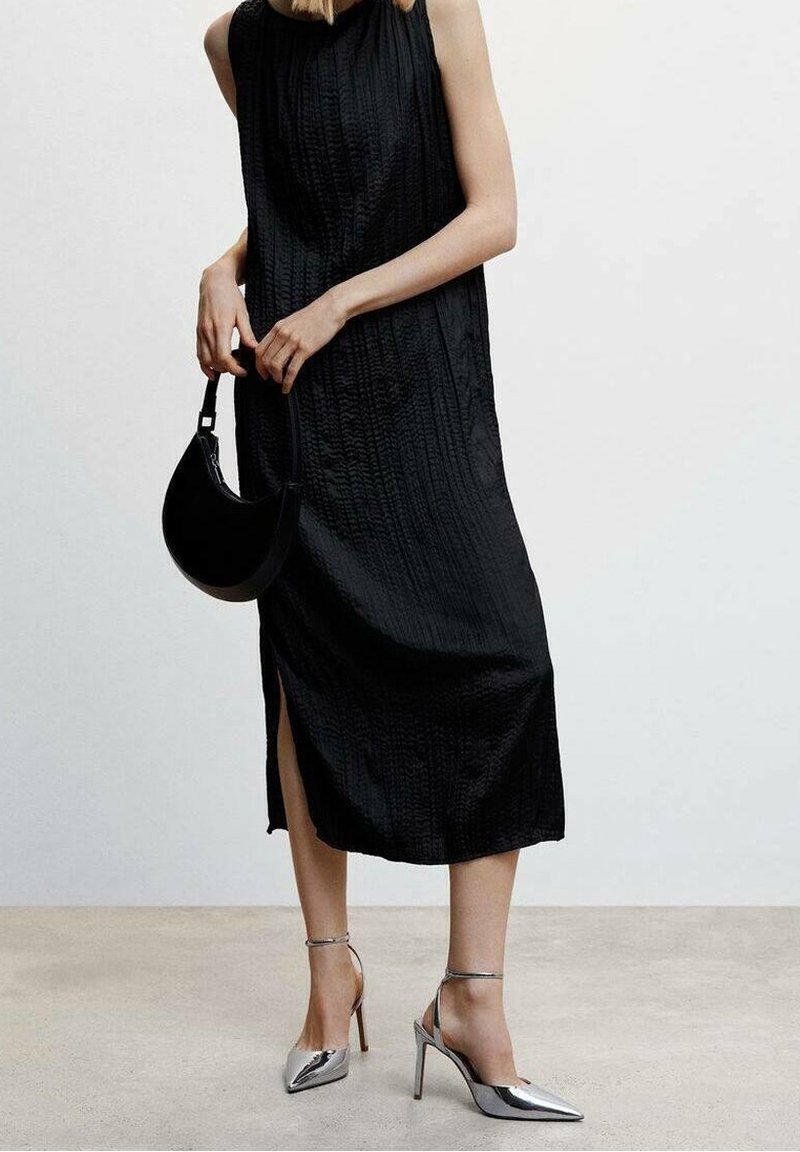 Vestido midi sin mangas, de textura negra y con una abertura lateral, combinado con tacones plateados de punta afilada y un bolso redondo negro.