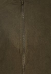 Giacca in pile verde oliva con zip frontale. Texture morbida con una superficie liscia e uniforme, senza motivi o decorazioni visibili.