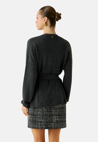 Maglione grigio lavorato a maglia con vita con cintura, caratterizzato da maniche lunghe e scollatura semplice, abbinato a una gonna testurizzata bianca e nera.