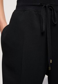 Czarne spodnie dresowe z elastycznym pasem ze sznurkiem, gładką fakturą, bocznymi kieszeniami i subtelnymi złotymi akcentami na końcówkach sznurków.