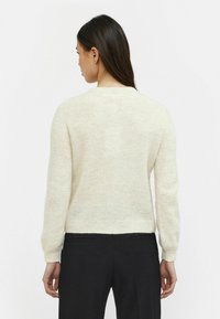 Crewneck trui in zacht, licht créme gebreid. Heeft aansluitende mouwen en een zoom, met een subtiele textuur. Draagt met zwarte broeken voor contrast.