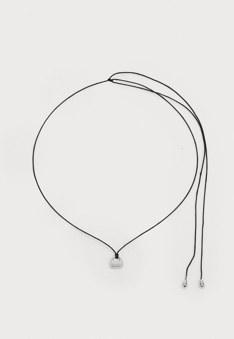 Juodasis virvelės kaklo papuošalas su mažą sidabro spalvos pakabuku, ant kurio išgraviruota "JUODAS". Dizainas apima du metalinius galus virvelėje.