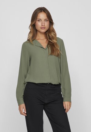 Oliven grøn langærmet blouse med v-hals, glat tekstur, frontknaplukning og sideslidser; parret med sorte bukser.