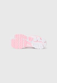 Semelle d'une chaussure de sport blanche et rose avec des semelles à motif en grille, placée sur un fond blanc uni.