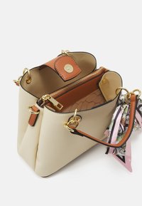 Borsa beige con texture, dotata di accessori in oro, una tracolla in pelle marrone, una tasca con zip e dettagli decorativi in nastro di seta.