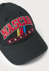 Svart baseballcaps med brodert "NASCAR" i rødt, med blå, gul og rød striper nedenfor. Mykt stoff med buet skjerm.