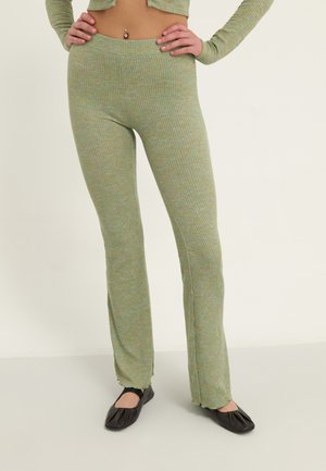 Pantalones acampanados de punto verde acanalado con una cinturilla sin costuras. La tela presenta un patrón multicolor y una textura suave.