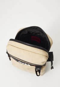 Zaino marrone realizzato in tessuto morbido, con chiusura a zip, dettagli neri e fodera interna visibile con etichetta rossa.