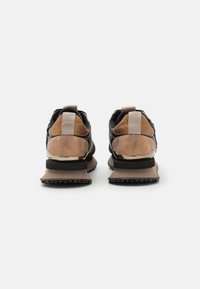 Zapatillas deportivas negras y marrones con materiales mixtos, que incluyen ante y malla. Presentan un collarín acolchado, una asa de tiro y una suela de goma texturizada.