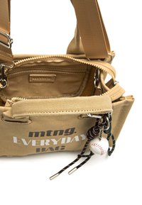 Beige Leinentasche mit silbernen Beschlägen, Reißverschluss und verstellbarem Riemen. Auf der Vorderseite bedruckter Text "mtng. EVERYDAY BAG", mit dekorativen Charms.