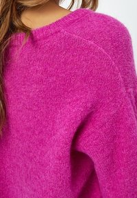 Sweter w fuksjowym kolorze wykonany na drutach o miękkiej fakturze, z szerokim dekoltem i rękawami raglanowymi. Tył prezentuje swobodny krój.