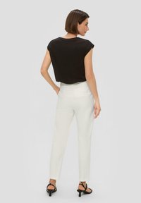 Zwarte top met kapmouwen, witte op maat gemaakte broek en zwarte sandaaltjes met bandjes. Gladde stof en aansluitende silhouet. Model toont de achterkant.
