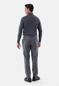 Graues langärmliges Poloshirt, kombiniert mit grauen strukturierten Anzughosen. Das Outfit wird mit dunkelbraunen Schuhen und dezenten Knopfdetails an den Hosen abgerundet.