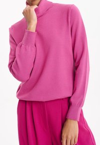 Rosa polotröja gjord av mjukt tyg, med långa ärmar och ribbade muddar. Bärs med matchande rosa byxor.