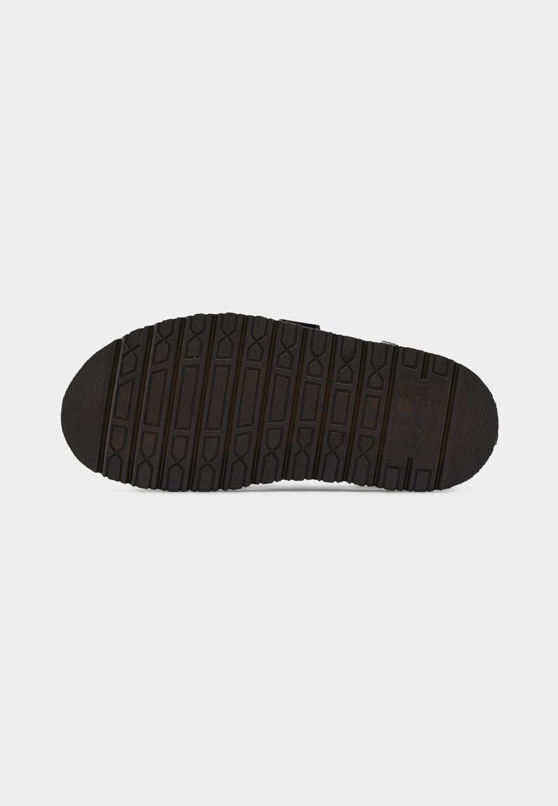 Black rubber shoe sole with horizontal and geometric tread patterns for traction and grip on flat surface.