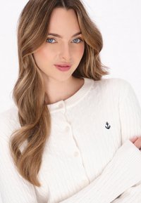Witte cable-knit cardigan met een ronde halslijn, knoopsluiting en kleine marineblauwe ankerborduursel op de borst.