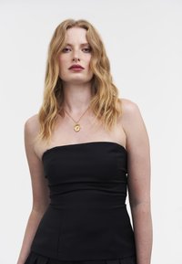 Zwarte strapless top met een aansluitend ontwerp, licht gestructureerde stof en zichtbare naden. Gecombineerd met een gouden hangersketting.