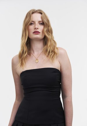 Črni top brez naramnic s prilegajočim se krojem, rahlo teksturirano tkanino in vidnimi šivi. Nošen z zlatim obeskom na verižici.