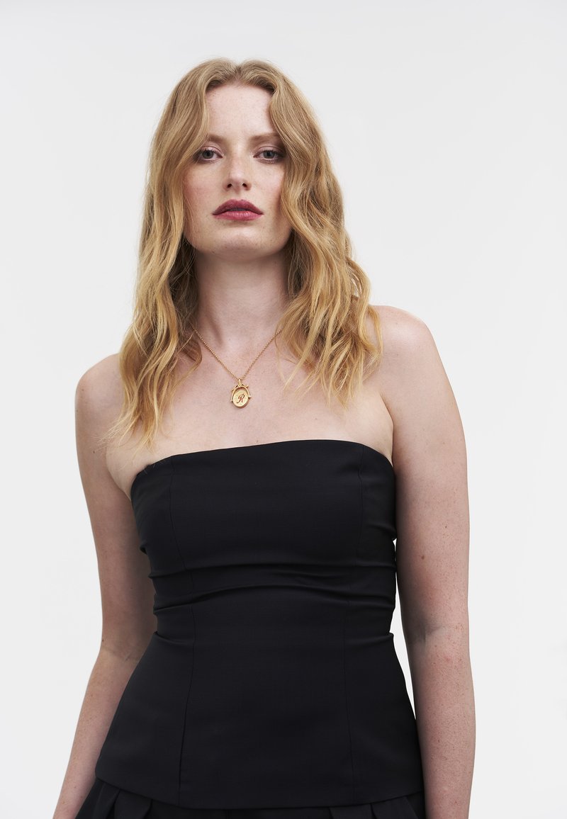 Zwarte strapless top met een aansluitend ontwerp, licht gestructureerde stof en zichtbare naden. Gecombineerd met een gouden hangersketting.