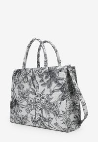 Bolsa de lona con diseño de flores negras y estampado de animales sobre un fondo gris claro, con dos asas y una correa desmontable.