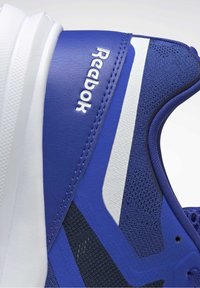 Modrá sportovní bota s síťovinou a syntetickým svrškem, bílými akcenty, texturovaným povrchem a vyraženým logem "Reebok" na boku.