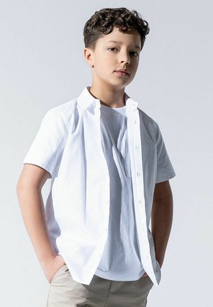 Biała koszula na guziki z krótkim rękawem, noszona na jasnoszarej koszulce, przedstawiona na jednolitym tle, z gładkim materiałem i luźnym krojem.