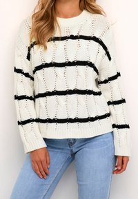 Pull en maille blanche avec des rayures noires horizontales, un motif torsadé texturé, et un col rond. Le modèle porte un jean bleu clair.