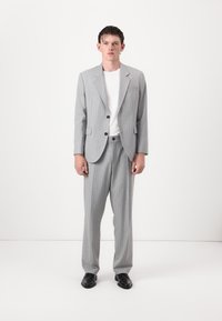 Gray pinstriped suit with a structured blazer and straight-leg trousers, paired with a white t-shirt and black shoes. Plain background.