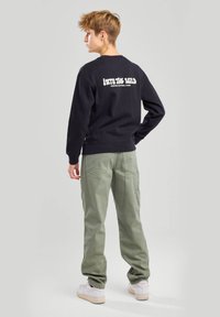 Musta puuvillainen collegepaita, jossa valkoiset tekstit "INTO THE WILD ARIZONA NATIONAL PARK" selässä, yhdistettynä oliivinvihreisiin cargo-housuihin ja valkoisiin lenkkareihin.