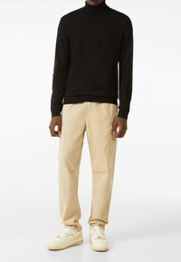 Svart stickad polotröja, beige cargobyxor med sidfickor, och krämfärgade sneakers med strukturerade sulor. Minimalistisk design, skräddarsydd passform.