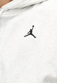 Μαύρο σιλουέτα λογότυπο ενός ατόμου που πηδάει με ένα εκτεταμένο χέρι κρατώντας μια μπάλα μπάσκετ σε λευκό υφασμάτινο φόντο.