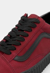 Sneaker rossa in suede con lacci neri e suola in gomma. Presenta una parte superiore liscia e testurizzata e un design a striscia laterale in contrasto.