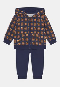 Tuta da ginnastica blu navy con felpa con zip caratterizzata da un motivo di orsi e miele, accompagnata da pantaloni abbinati. Realizzato in tessuto morbido con polsini a coste.