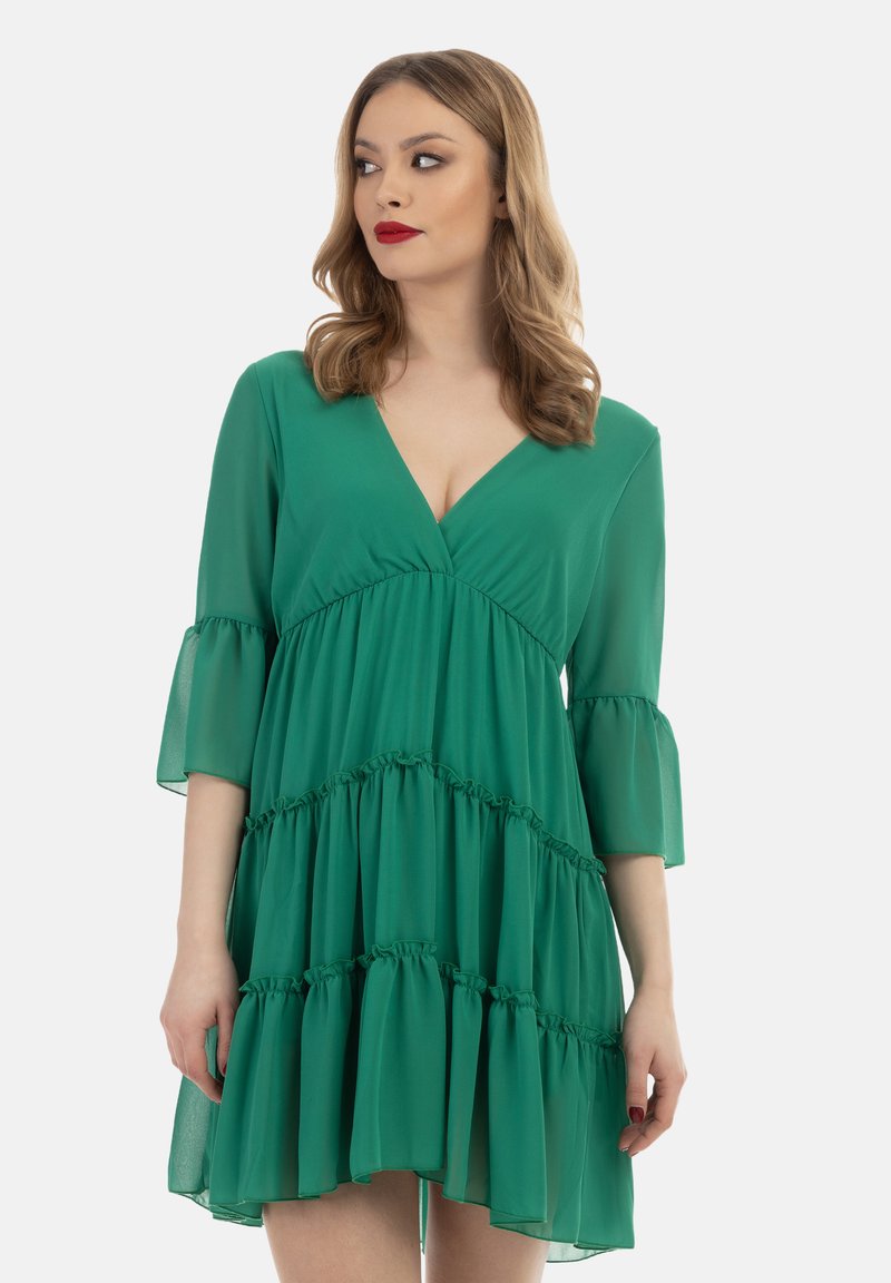 Rochie verde din chiffon cu decolteu în V, mâneci evazate și design cu volane în straturi. Material ușor, până la genunchi și textură netedă.