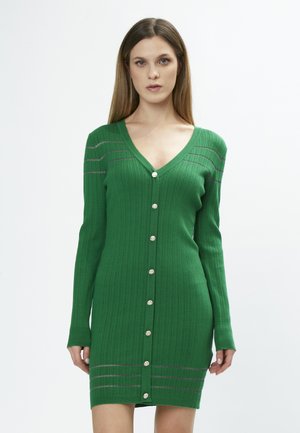 Robe-cardigan en tricot vert avec un décolleté en V, des manches longues, un jeu de côtes verticales, des boutons argentés et des rayures horizontales grises aux épaules.