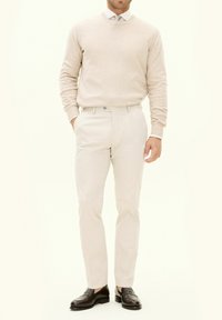 Beige Strickpullover, hellbeige Hose, braune Slipper. Der Pullover hat einen runden Ausschnitt, die Hose ist tailliert mit flachem Bund und Taschen.