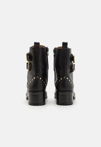 Sorte skinnankelstøvler med gullhardware, med to sidelåser og naglede detaljer på baksiden. Kraftig hæl, glatt tekstur.