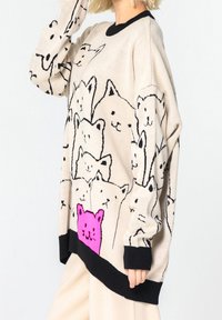 Maglione a maglia beige con contorni di gatti neri e un design prominente di un gatto rosa all'orlo, con polsini e fondo a costine neri.