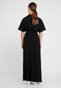 Black maxi dress with a relaxed fit, short sleeves, and a fitted waist, crafted from soft fabric; worn with white shoes.