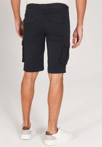 Shorts cargo noirs avec plusieurs poches latérales, en matériau coton, coupe droite et taille régulière, associés à des baskets blanches.