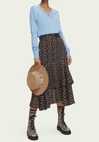 Himmelblauer V-Ausschnitt-Pullover, schwarzer floraler Stufenrock, beiger Hut mit gemustertem Band und gemusterte Combat-Boots mit Schnürsenkeln.